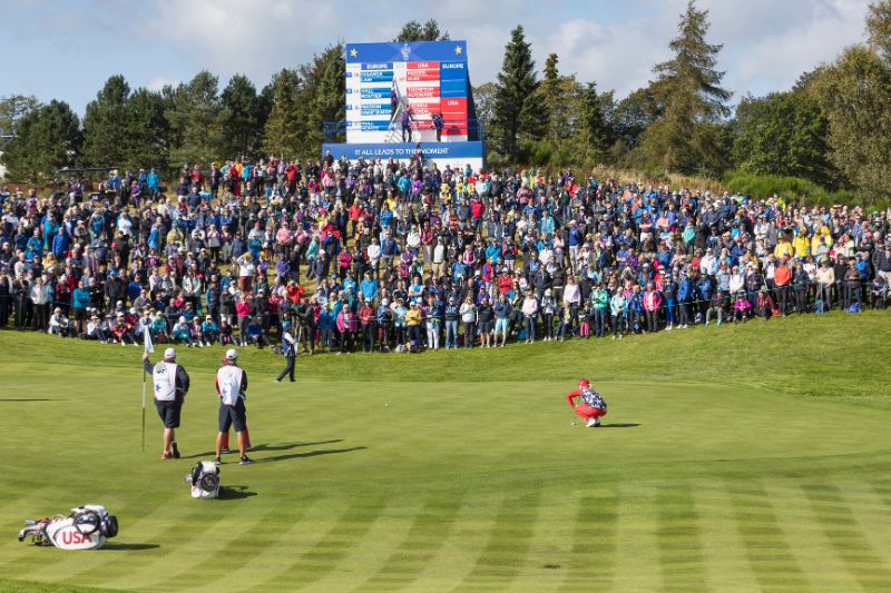 People playing golf in front of a large crowd in Scotland