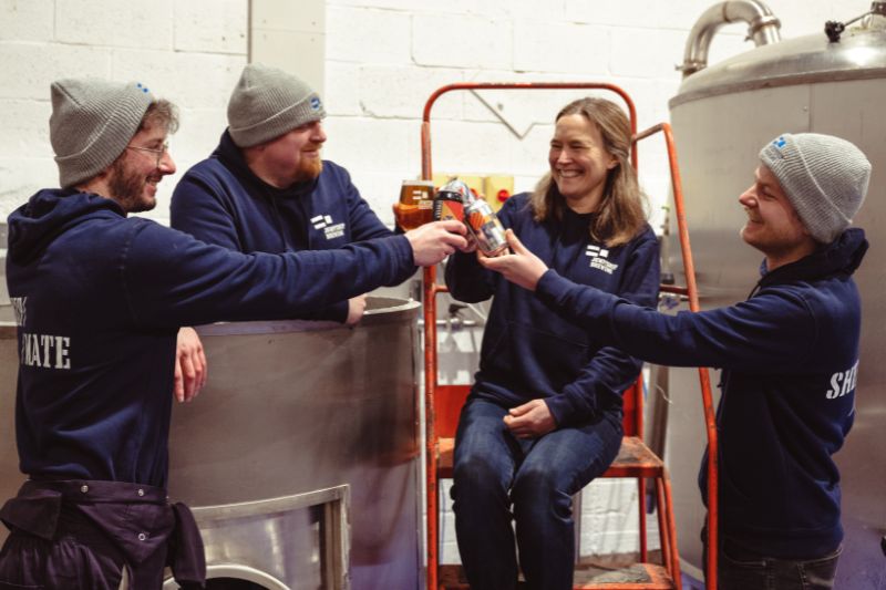 Four people smiling and holding up cans of Jump Ship beer