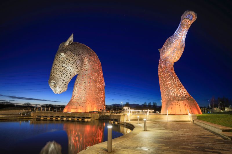 The Kelpies at Helix Park in Scotland lit up at night 